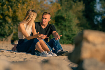 A young man quarrels with his girlfriend who turns away from him offended while sitting on sandy...