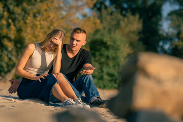 A young man quarrels with his girlfriend who turns away from him offended while sitting on sandy...