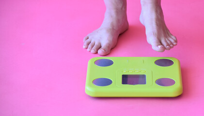 Caucasian bare feet standing on scale to measure weight,pink background. Control of weight, dieting and overweighting. 