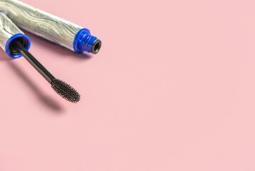 Black mascara in silver tube on pink background