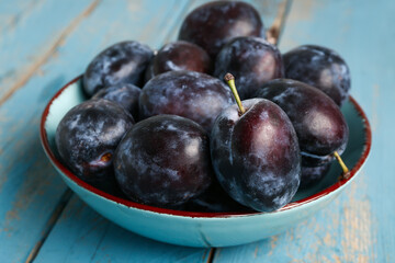 Bowl with fresh plums on blue wooden background