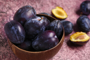 Bowl with fresh plums on purple background