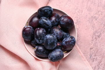 Bowl with fresh plums on pink background