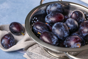 Colander with fresh plums on blue background
