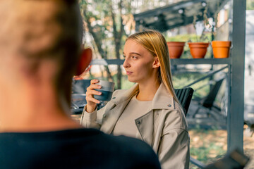 A young beautiful girl drinks tea and talks with her boyfriend while sitting on the terrace near a...
