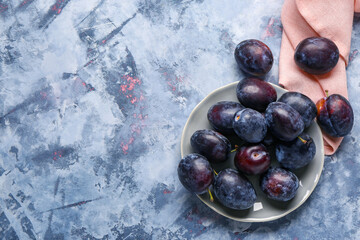 Plate with fresh plums on blue background