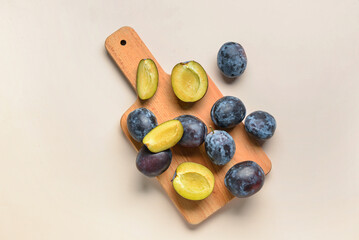 Wooden board with fresh plums on beige background