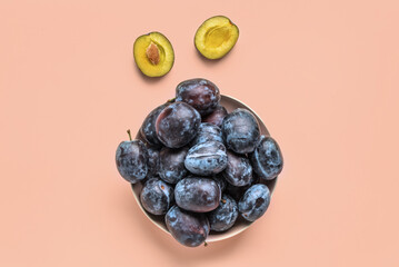 Bowl with fresh plums on pink background
