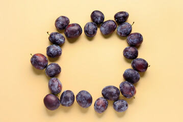 Frame made of fresh plums on yellow background
