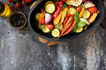 Grilled vegetables: red and yellow paprika, garlic, zucchini, eggplants, carrots in a frying pan on a dark stone background. View from above. Copy space.