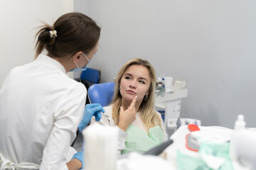 a female dentist talking to patient sad girl complaining of tereble toothache, holding her jaw in the clinic