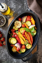 Grilled vegetables: red and yellow paprika, garlic, zucchini, eggplants, carrots in a frying pan on a dark stone background. View from above.