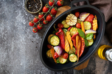 Grilled vegetables: red and yellow paprika, garlic, zucchini, eggplants, carrots in a frying pan on a dark stone background. View from above. Copy space.