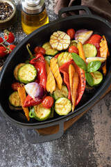 Grilled vegetables: red and yellow paprika, garlic, zucchini, eggplants, carrots in a frying pan on a dark stone background. Copy space.