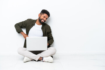 Young Brazilian man with a laptop sitting on the floor isolated on white suffering from backache for having made an effort