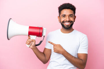 Young Brazilian man isolated on pink background holding a megaphone and pointing side