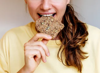Fotobehang Woman eating grain bread close-up. Healthy eating and diet background. © Barillo_Picture