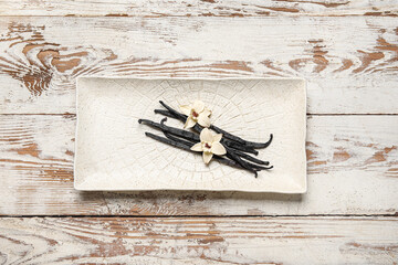 Plate with aromatic vanilla sticks and flowers on white wooden background