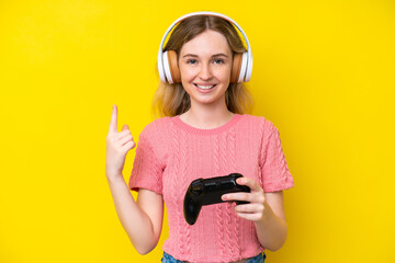 Blonde English young girl playing with a video game controller isolated on yellow background...