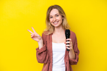 Young singer caucasian woman picking up a microphone isolated on yellow background smiling and...