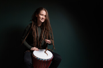 Percussion musician. Pretty young woman playing djembe. Green background.