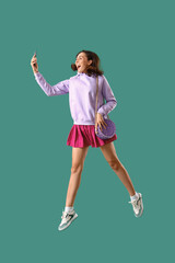 Young woman in lilac hoodie with mobile phone jumping on green background