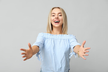 Young woman opening arms for hug on grey background