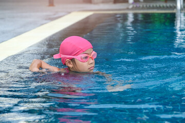 Little girl plays in the outdoor swimming pool of tropical resort during family summer vacation. Kids learning to swim. Healthy Summer Activities for Kids.