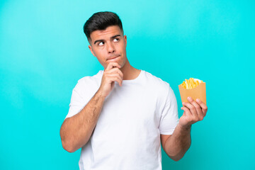 Young caucasian man catching french fries isolated on blue background having doubts and thinking
