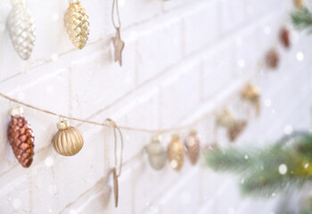 Glass Christmas toys on a jute rope hang on a white brick wall - a festive loft-style decor, a New Year mood. copy space