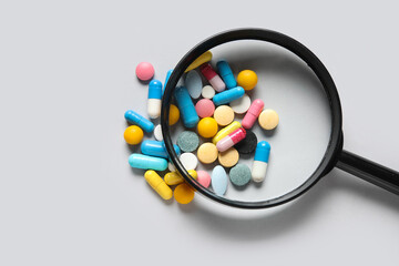 Magnifier with different pills on grey background