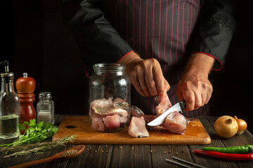 The cook cuts the raw fish into steaks and then cooks the herring in a jar. Working environment on the kitchen table with aromatic spices and pepper