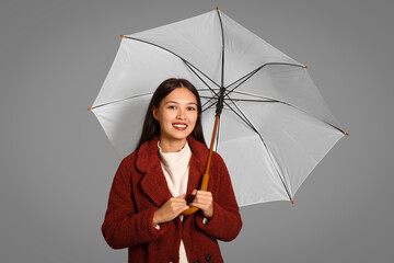 Beautiful young Asian woman with umbrella on grey background