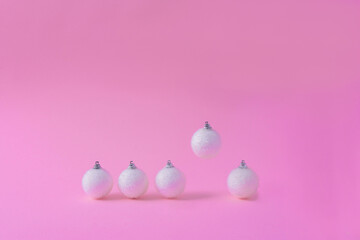 Creative layout made with a white Christmas bauble and a flying one on a pink pastel background. Minimal holiday decoration.