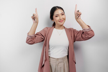 Excited Asian woman employee wearing cardigan pointing at the copy space above her, isolated by...
