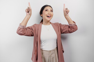 Excited Asian woman employee wearing cardigan pointing at the copy space above her, isolated by...