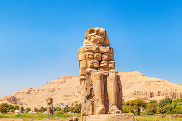 Famous  Colossi of Memnon - massive ruined statues of the Pharaoh Amenhotep III. Travel and tourist landmarks. Luxor, Egypt - October 21, 2023.