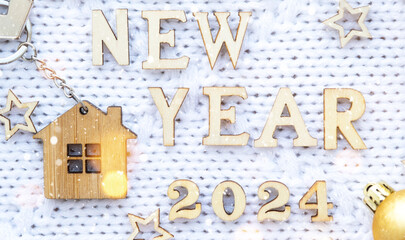 House key with keychain cottage on cozy festive knitted background with stars, bokeh. Happy New Year 2024 wooden letters, greeting card. Purchase, construction, relocation, mortgage, insurance