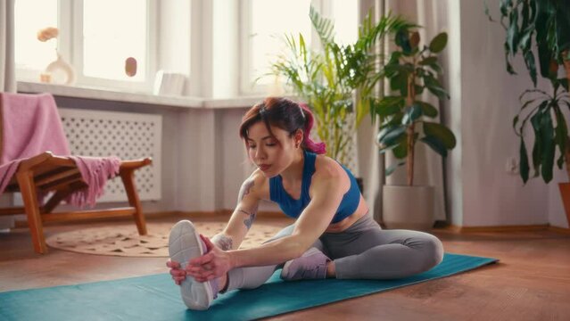 Young Asian woman with tattoos in sportswear exercising at home in the living room on a rubber mat. Sports, yoga and active lifestyle.