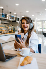 Beautiful and happy young woman sitting and eating delicious rolls in bakery or fast food. She also...