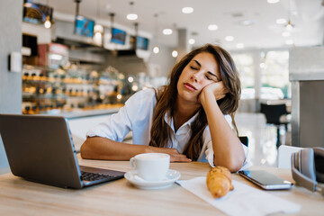 Beautiful and happy young woman sitting and eating delicious rolls in bakery or fast food while she...