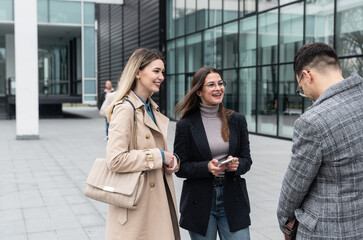 Group of successful young business people, leaders in marketing and motivation, stand in front of office building and consult before a meeting with employees. HR communication in companies concept