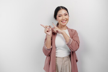 Fototapeta premium Excited Asian woman employee wearing cardigan pointing at the copy space beside her, isolated by white background