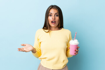 Young Uruguayan woman with strawberry milkshake isolated on blue background with surprise facial...