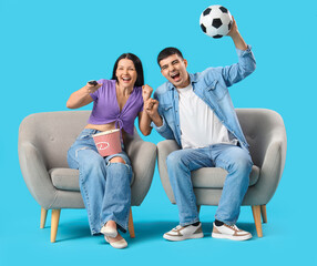 Cheerful young couple watching soccer match on TV against blue background