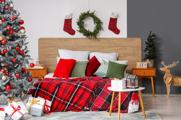 Interior of festive bedroom with cozy bed, Christmas tree, gift boxes and plaid blanket