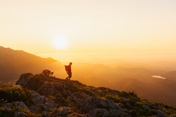 young man with backpack hiking with his border collie dog in the high mountains at sunset. sport, adventure and outdoor leisure.