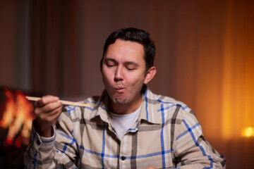 Young man eating sushi from home delivery pointing and showing with thumb up to the side with happy...