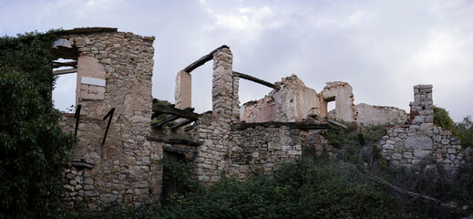 Abandoned Farmhouse in Ruins Amidst Overgrown Greenery with Forest and Mountains in the Background...