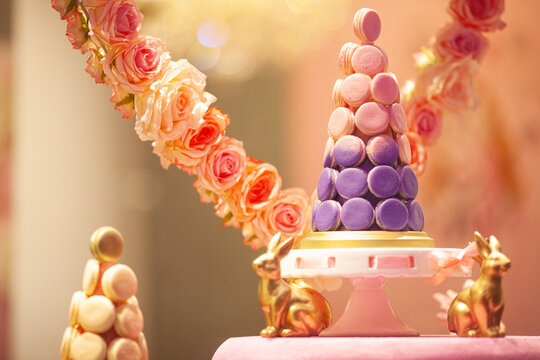 Pyramid, cone made of french macarons on pedestal cake plate, decorated with roses. Window of sweet shop. Close up. Indoor shot